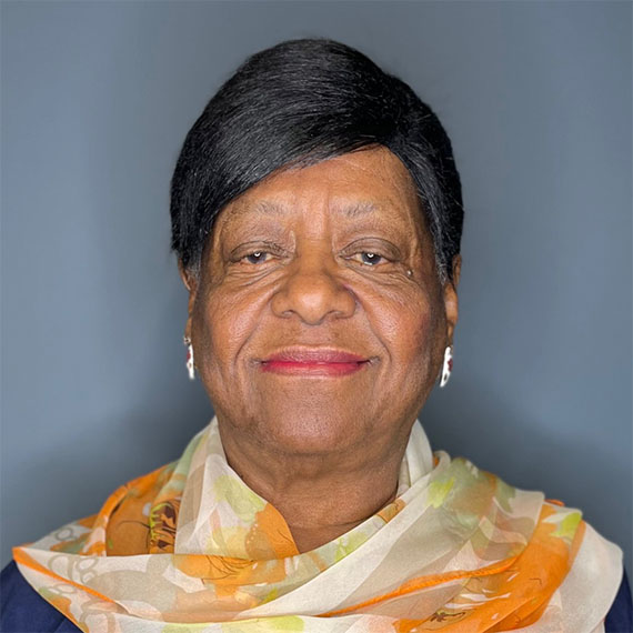Older black woman with short dark hair, wearing a yellow and orange scarf over a dark shirt